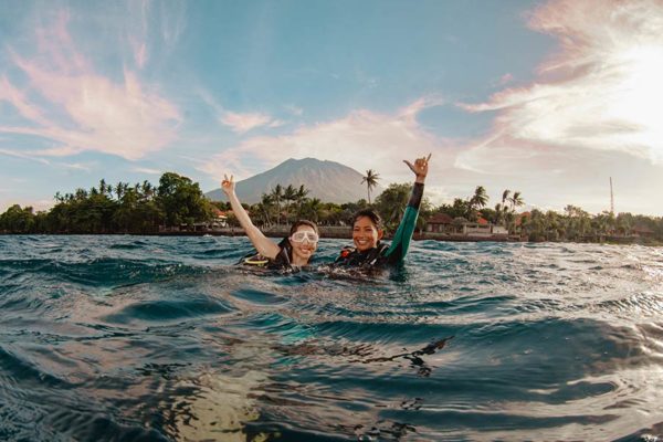 Scuba divers in the water in Tulamben, Bali with Mt Agung and the beach in the background.